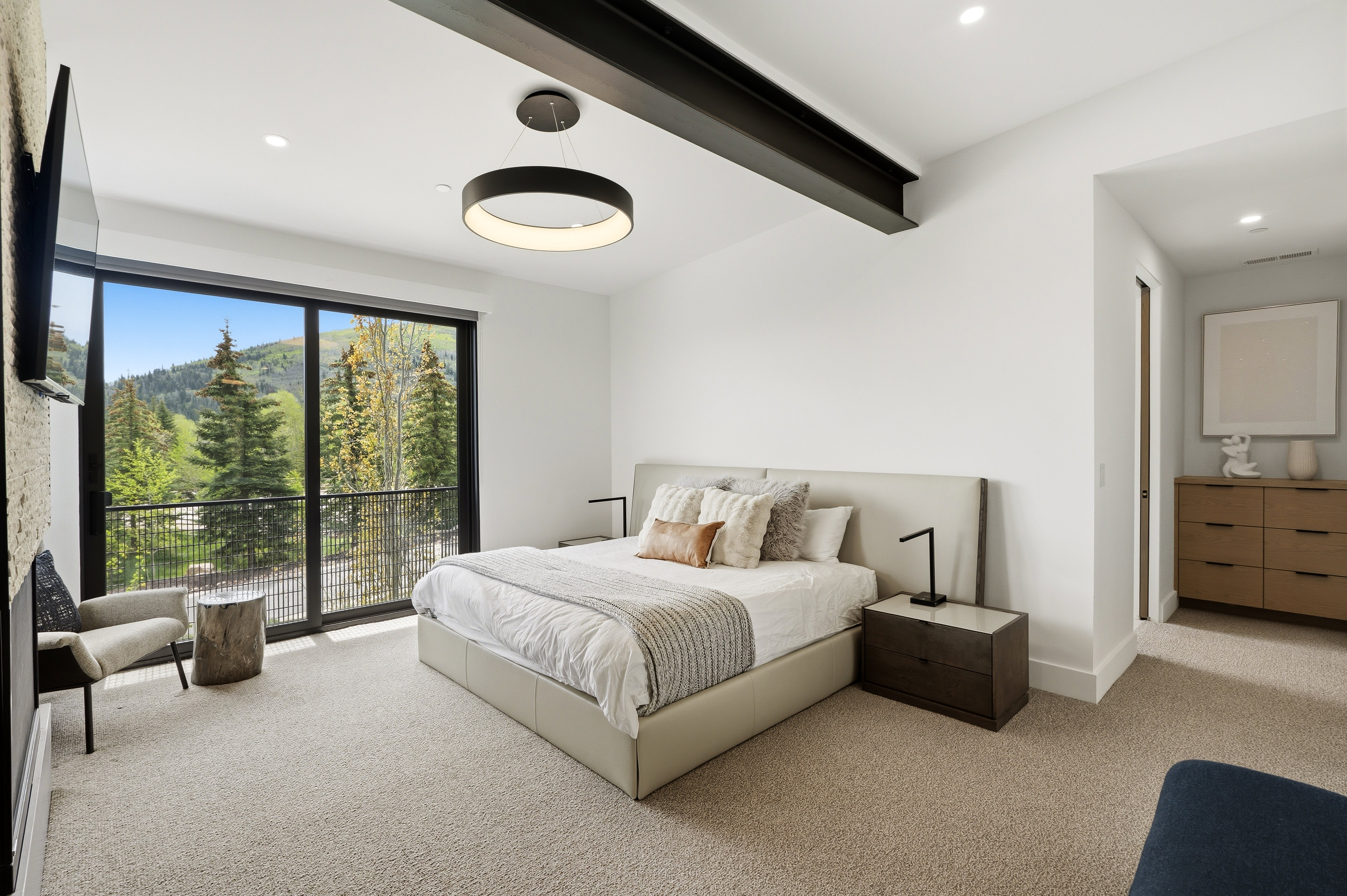 Spacious room featuring a floor-to-ceiling glass sliding door, leading to a private balcony with mountain and tree scenery