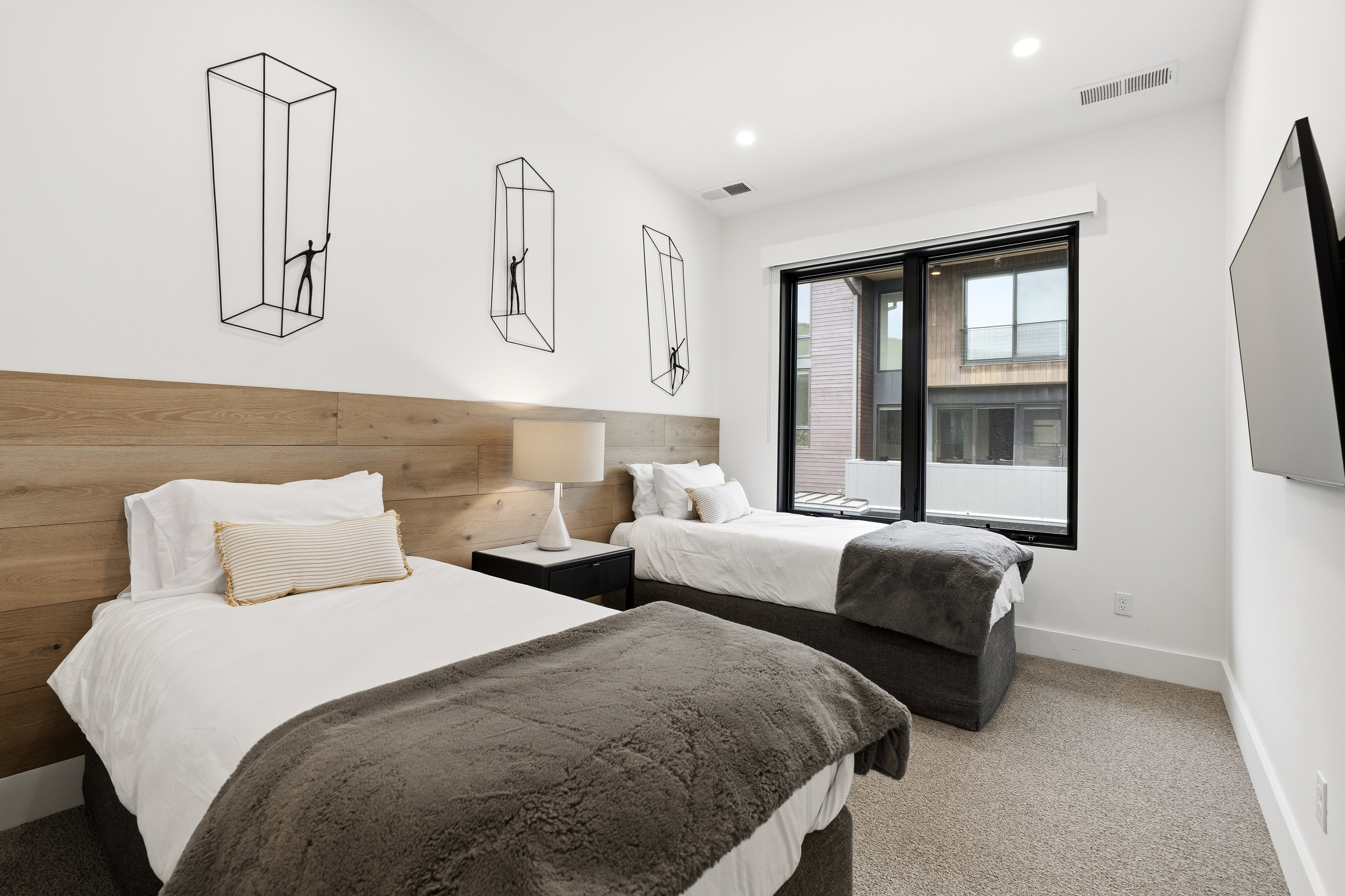 Spacious room featuring wood-finish accent wall, large window with black trim, recessed lighting, and light-toned carpet flooring