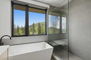 Freestanding soaking tub with a matte black faucet, set against a window with mountain and tree scenery