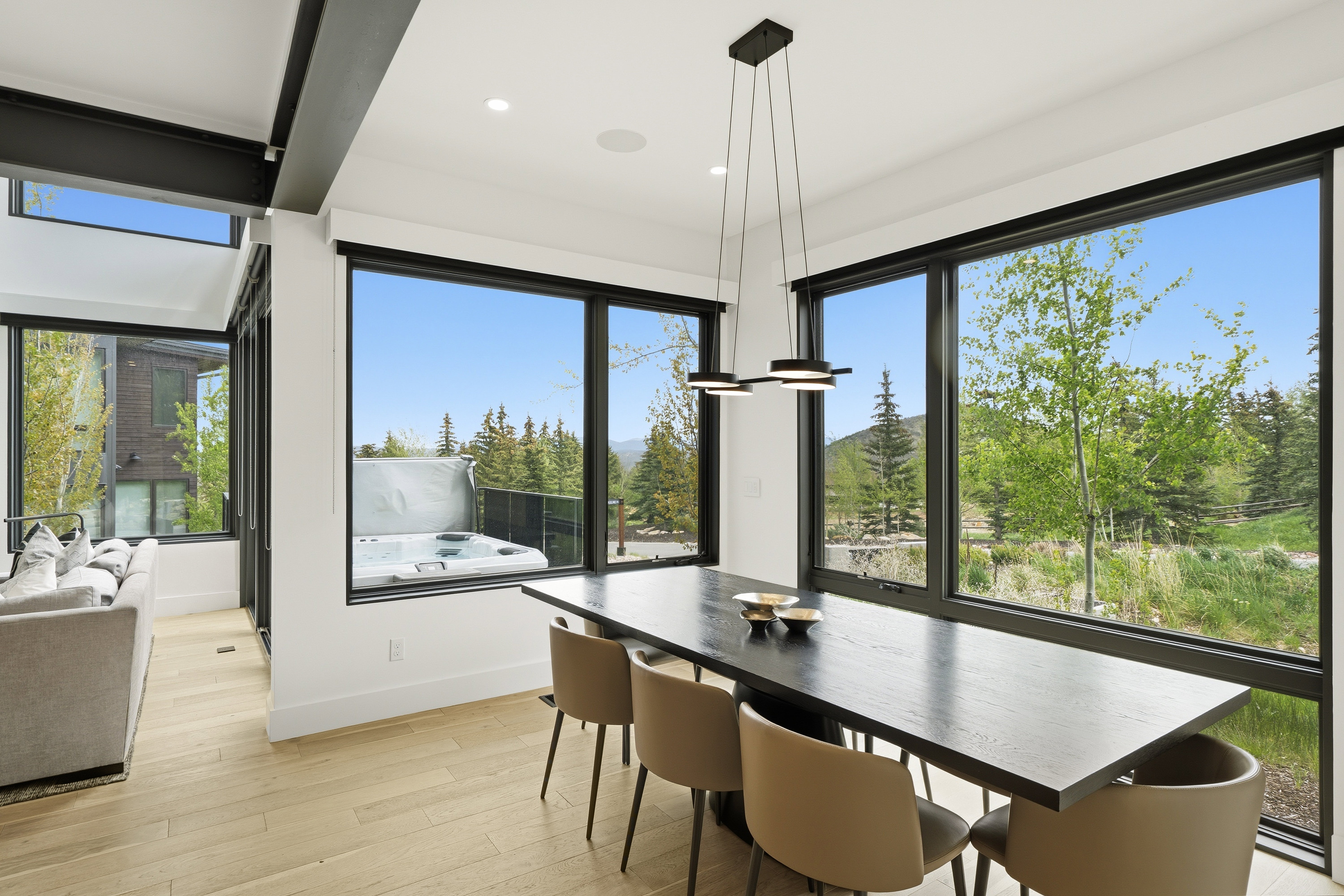 Open-concept dining area featuring light wood-finish flooring, a contemporary linear chandelier, and expansive windows