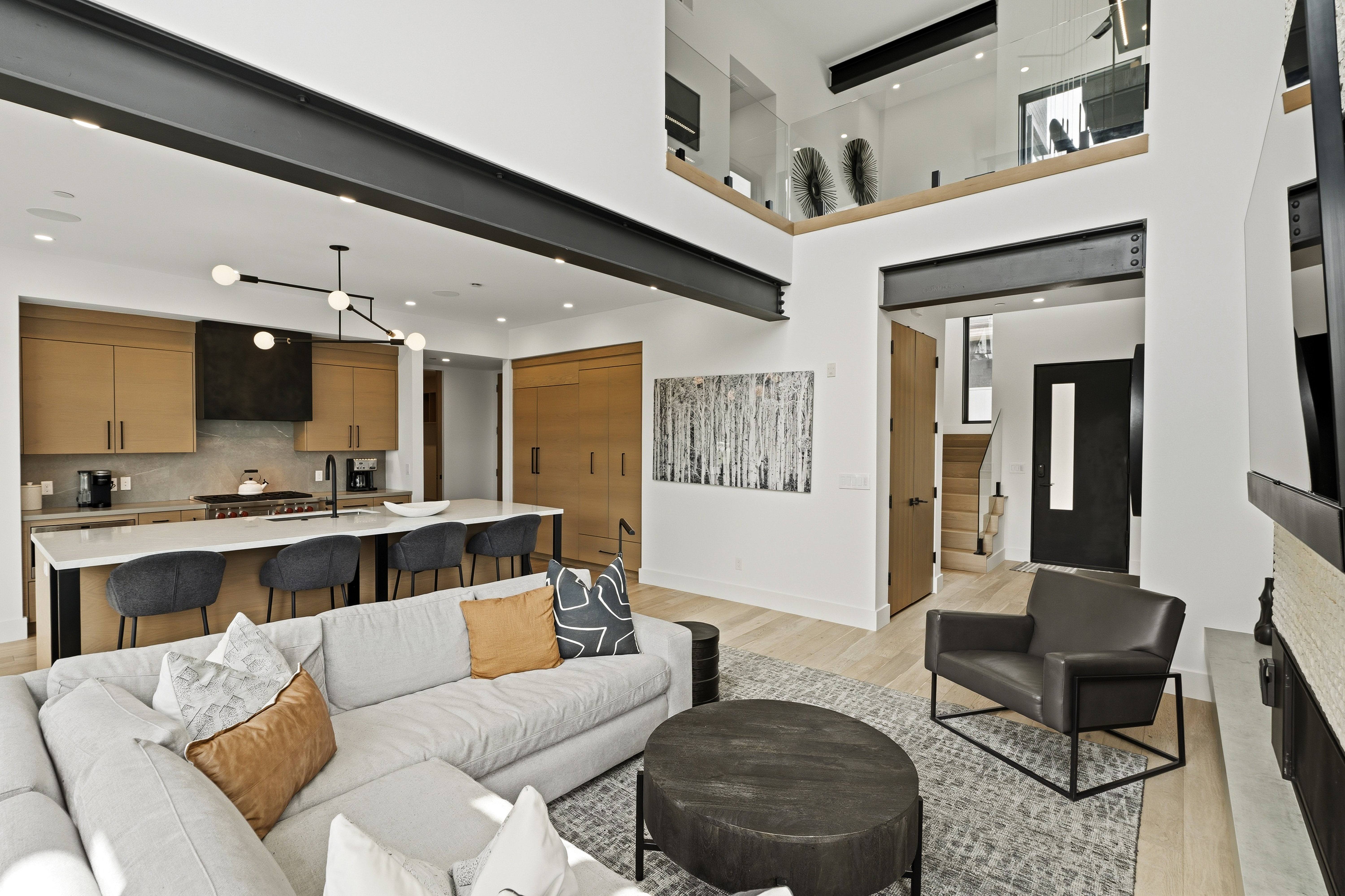 Open-concept living space featuring a double-height ceiling, exposed structural beams, and light wood-finish flooring