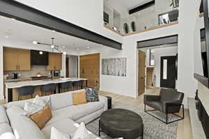 Open-concept living space featuring a double-height ceiling, exposed structural beams, and light wood-finish flooring