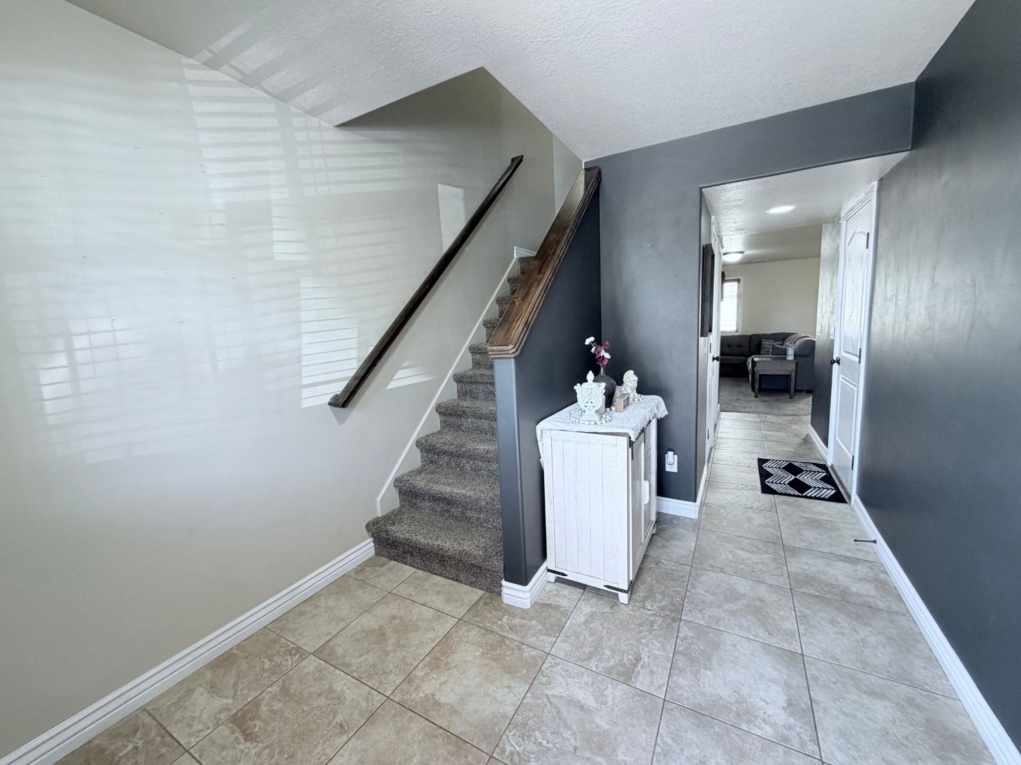 Entryway featuring neutral-toned tile flooring and a carpeted staircase with a dark wood handrail