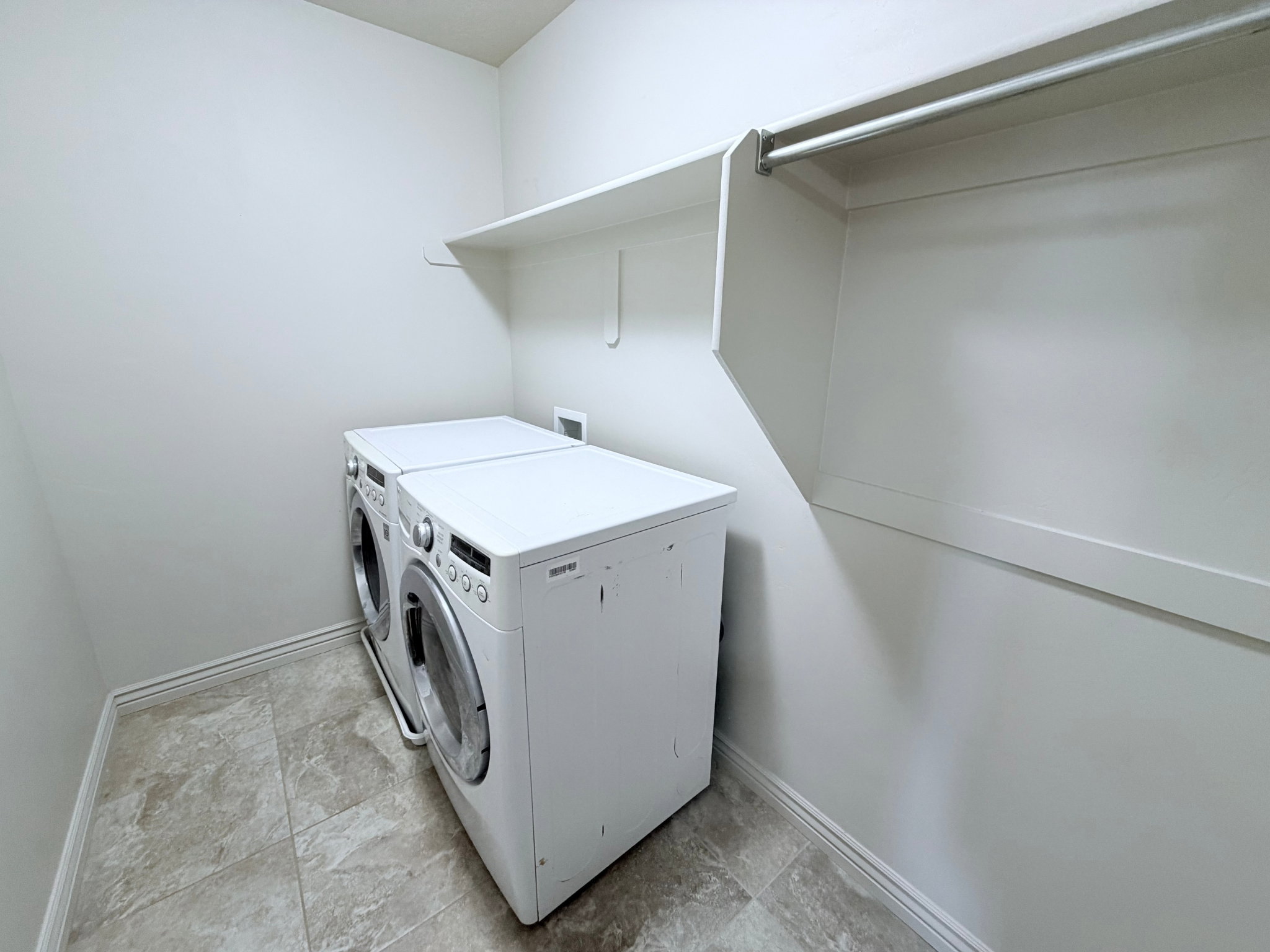Dedicated laundry area featuring a front-loading washer and dryer set, tile flooring, built-in shelving, and a hanging rod for convenience