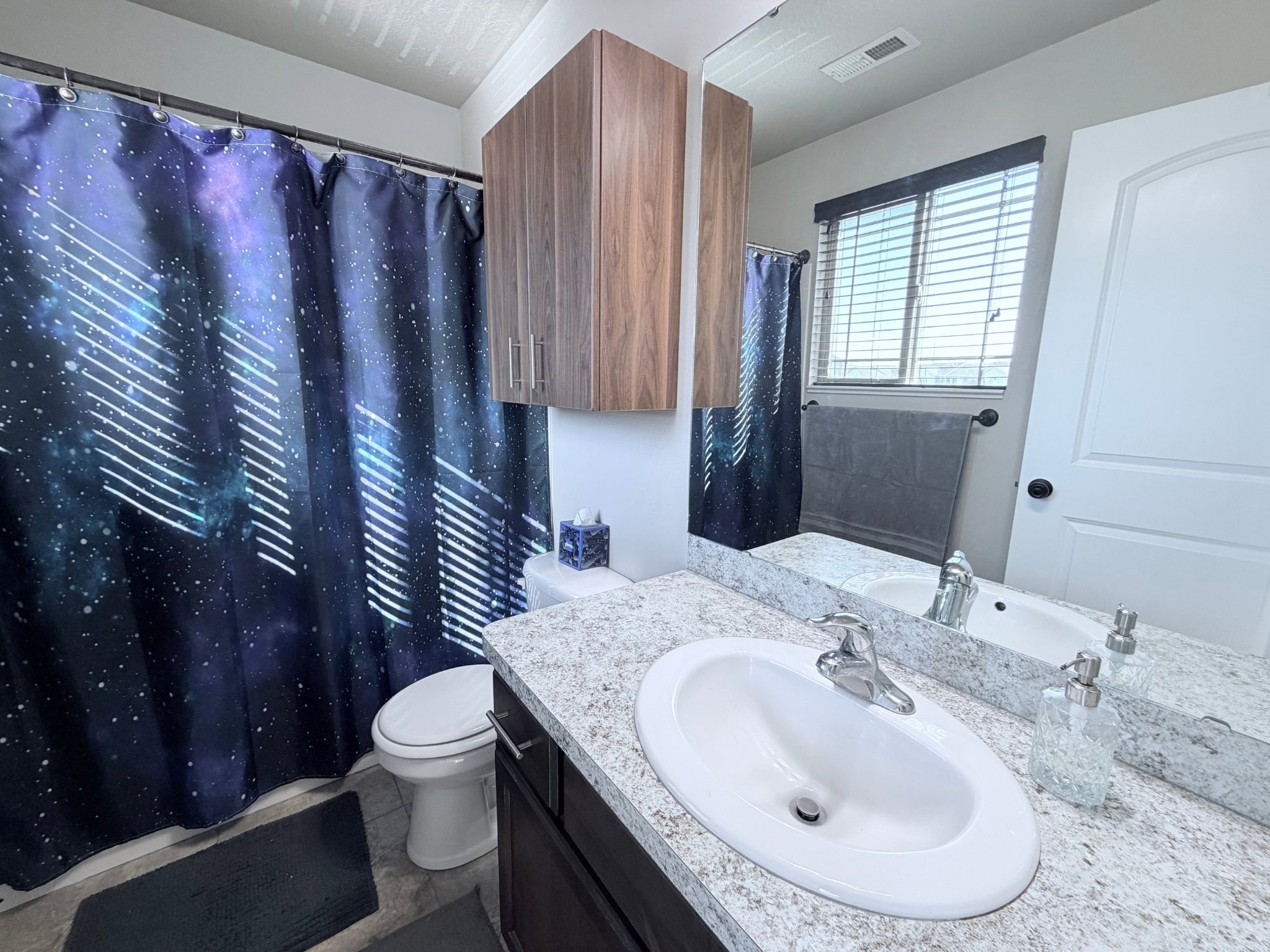En-suite bathroom featuring a single vanity with an integrated sink, a light speckled countertop, and dark wood-finish cabinetry