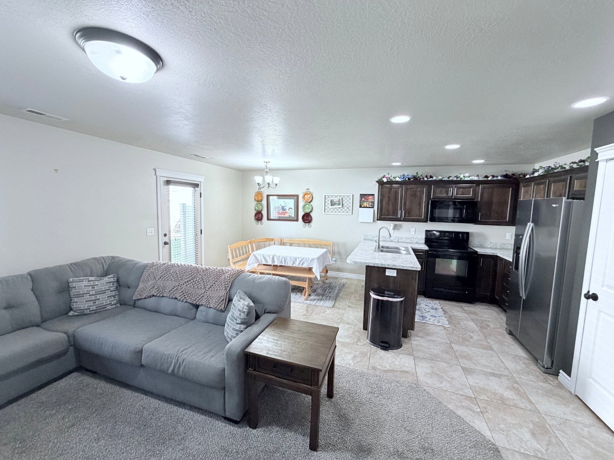 Open-concept living space featuring a kitchen with dark cabinetry, light-toned countertops, stainless steel appliances and an island
