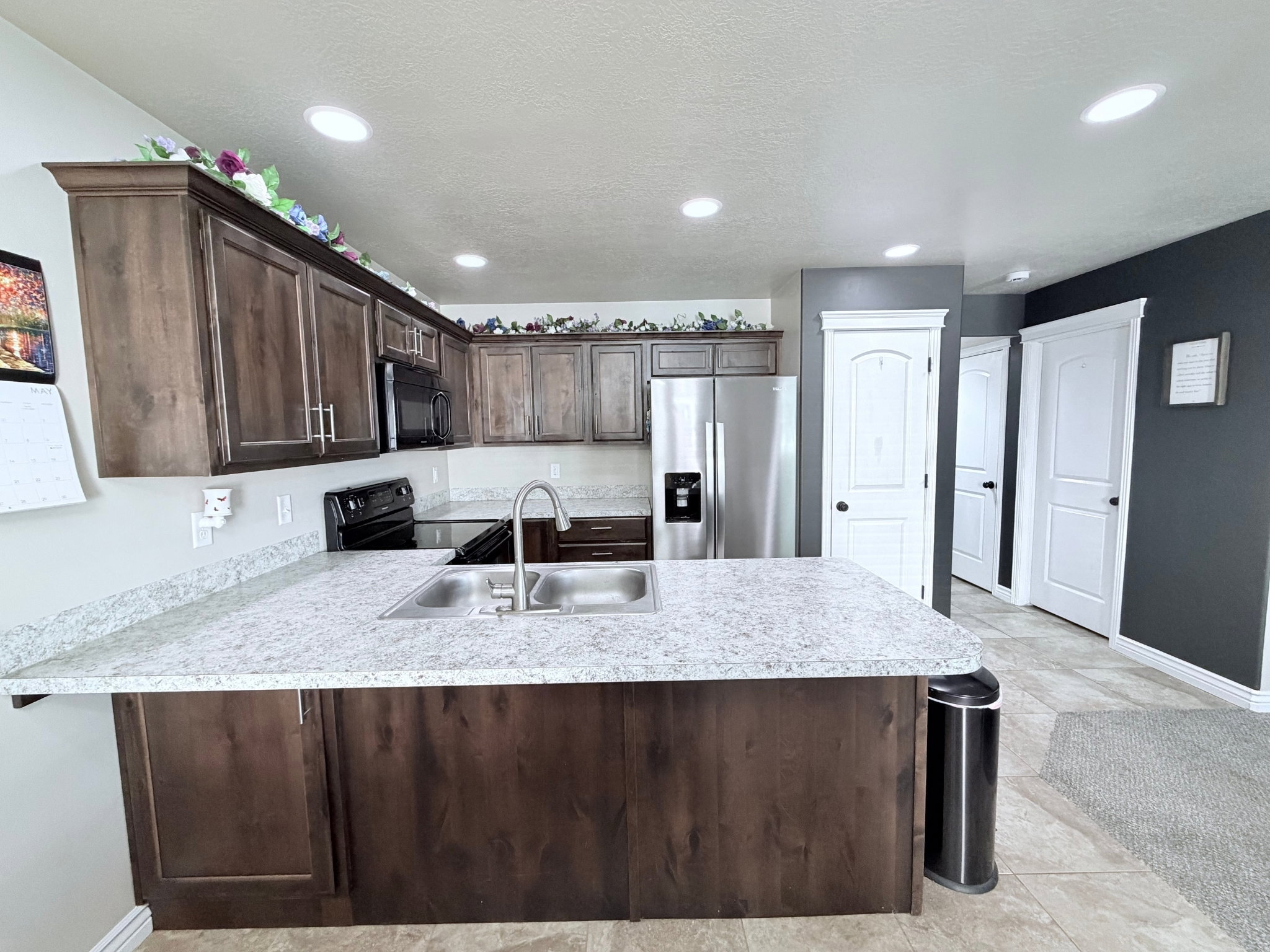 Kitchen featuring a large island with a double basin sink, dark wood-finish cabinetry, light countertops, and recessed ceiling lighting