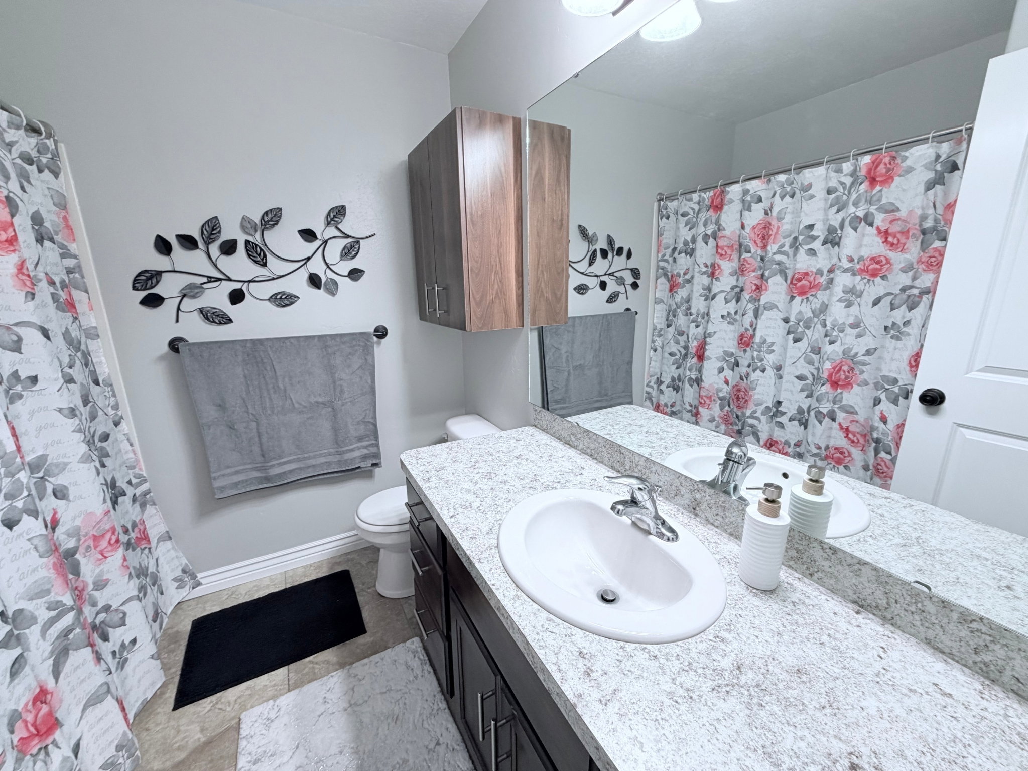 Bathroom #3 with a vanity featuring a white oval sink, light countertop, dark cabinetry and expansive wall-mounted mirror