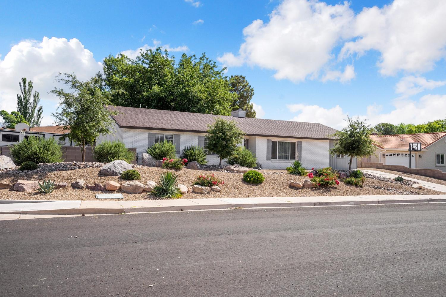 Ranch-style exterior with white brick facade, brown roof, and grey shutters
