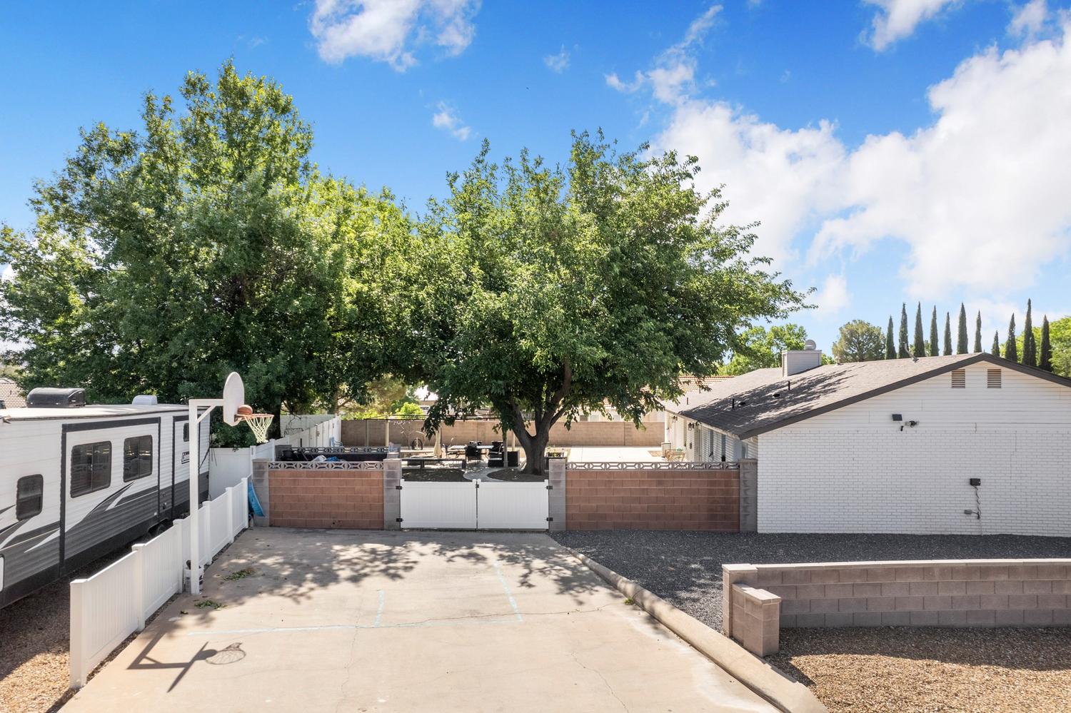 Expansive concrete pad, large mature trees, and a basketball hoop