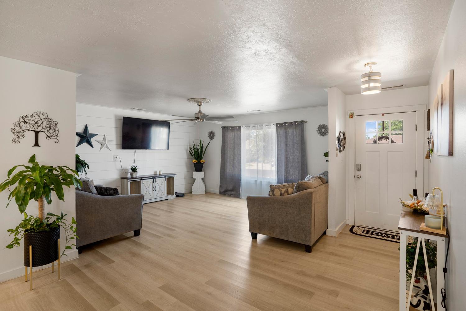 Bright interior featuring wood-finish flooring, a white paneled accent wall, and a ceiling fan with integrated lighting
