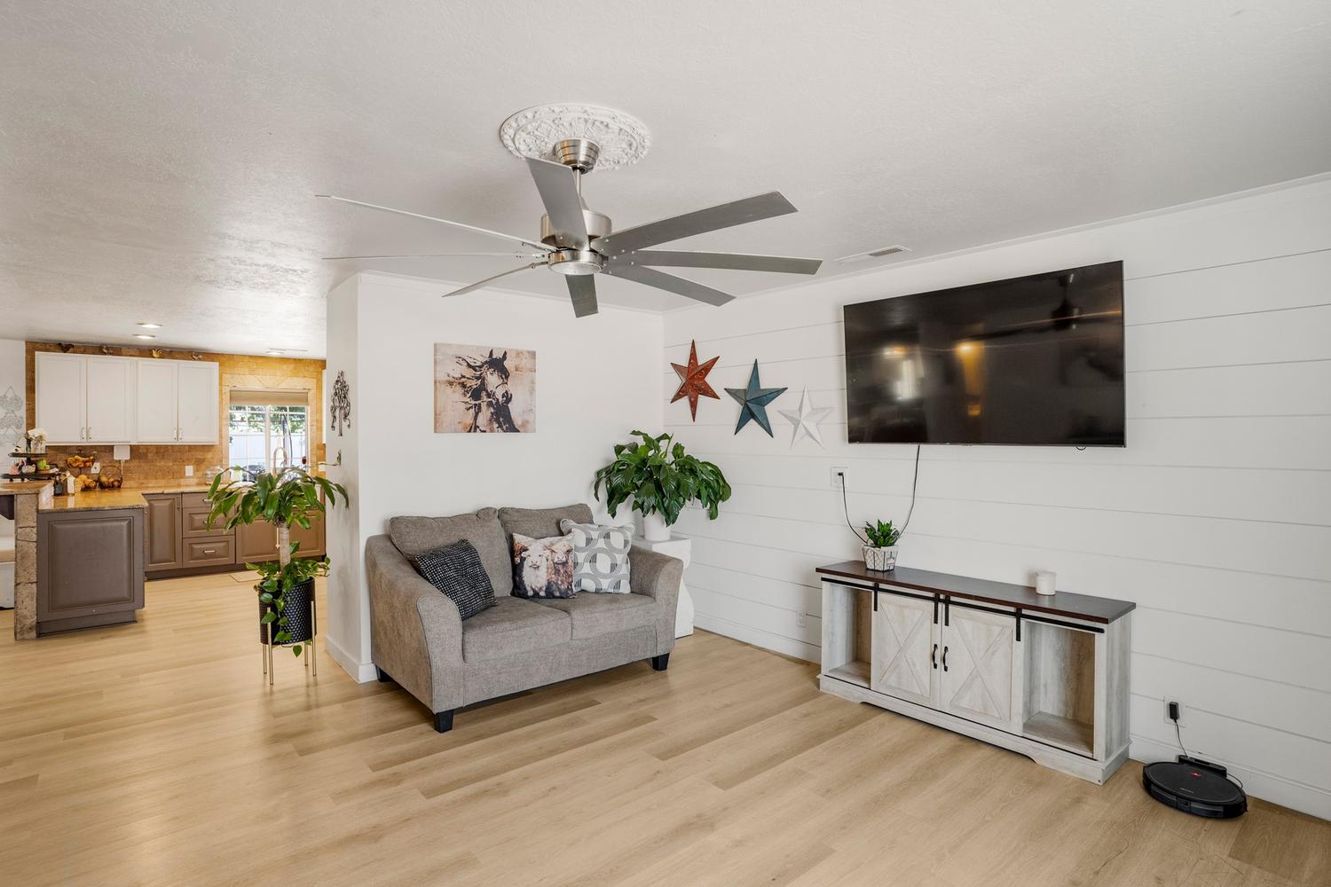 Living space featuring light wood-finish flooring, a contemporary ceiling fan with decorative medallion, and a white shiplap accent wall