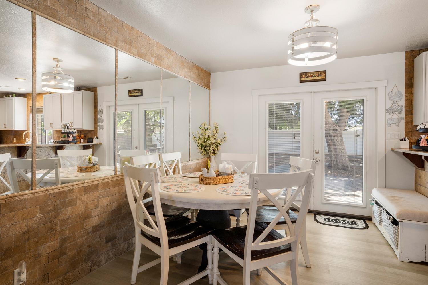 Dining area featuring French doors, a contemporary ceiling light fixture, wood-finish flooring, and a stone-clad half wall with integrated mirror panels