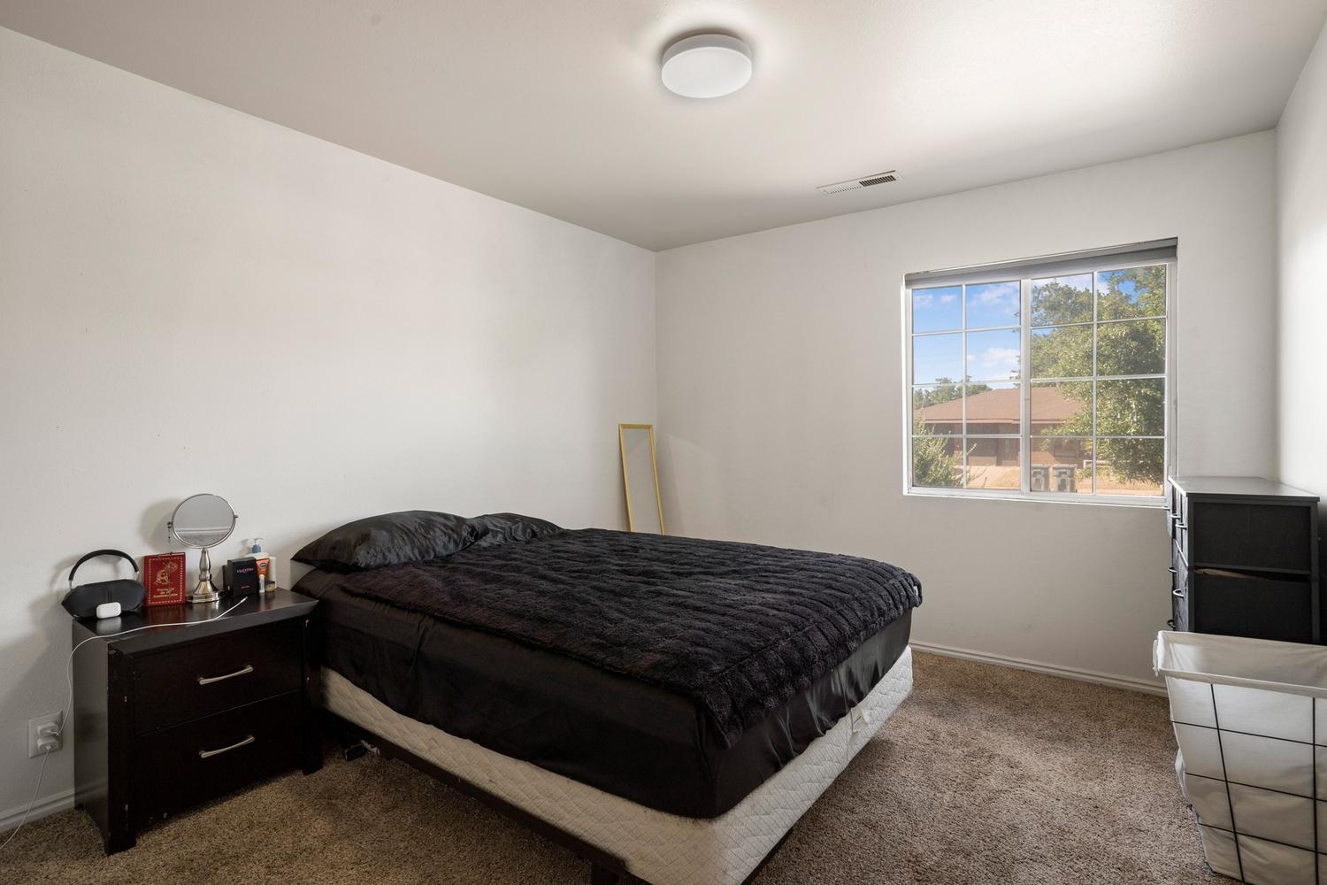 Bedroom featuring a large window, neutral-toned walls, brown carpet flooring, and a flush-mount ceiling light fixture