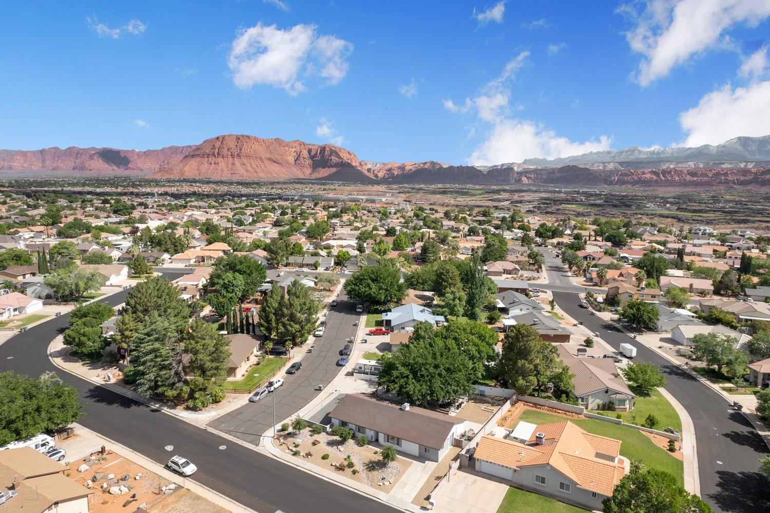 Expansive neighborhood featuring mature trees and paved streets, framed by distant red rock formations and mountain ranges