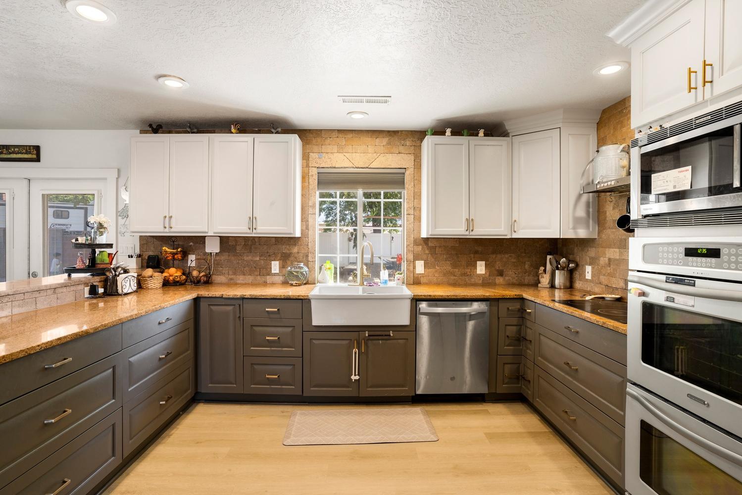 Kitchen featuring wood-finish flooring, two-tone cabinetry, a farmhouse sink, stainless steel appliances, and stone countertops