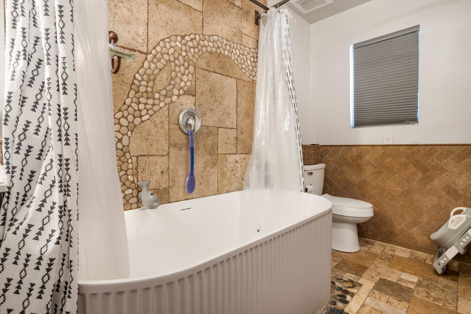 Freestanding bathtub with fluted paneling, set against a stone tile wall featuring a pebble mosaic detail