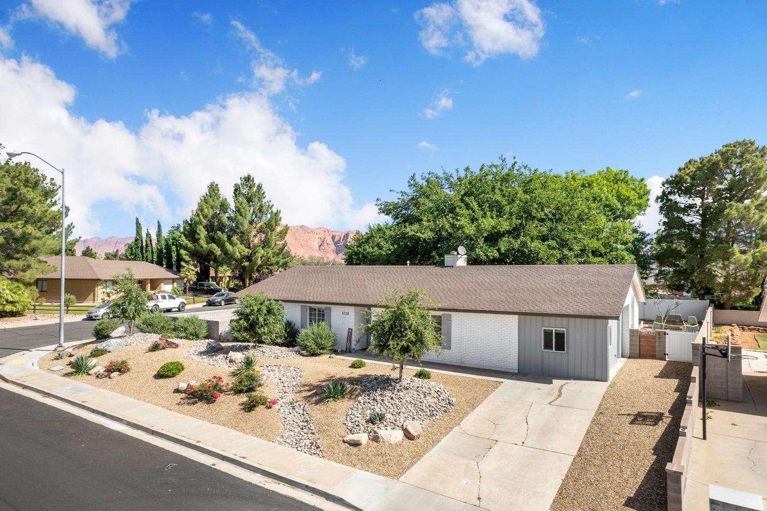 Single-story residence featuring a two-tone exterior, a concrete driveway, and a gravel front yard with mature landscaping
