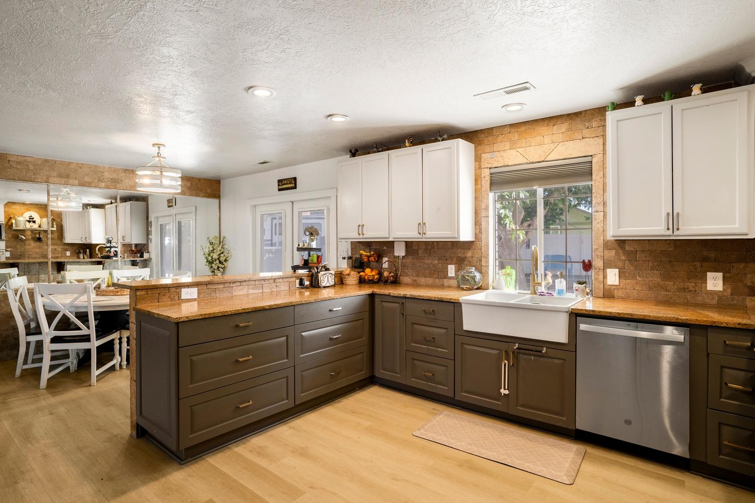 Spacious kitchen featuring two-toned cabinetry, a farmhouse sink, stainless steel dishwasher, and stone-finish countertops