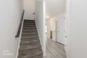 Carpeted staircase with dark wood-finish handrail, light wood-finish flooring, white walls, and white interior doors