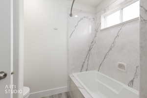 Bathtub with a marble-patterned surround, recessed shower niche, and an integrated window