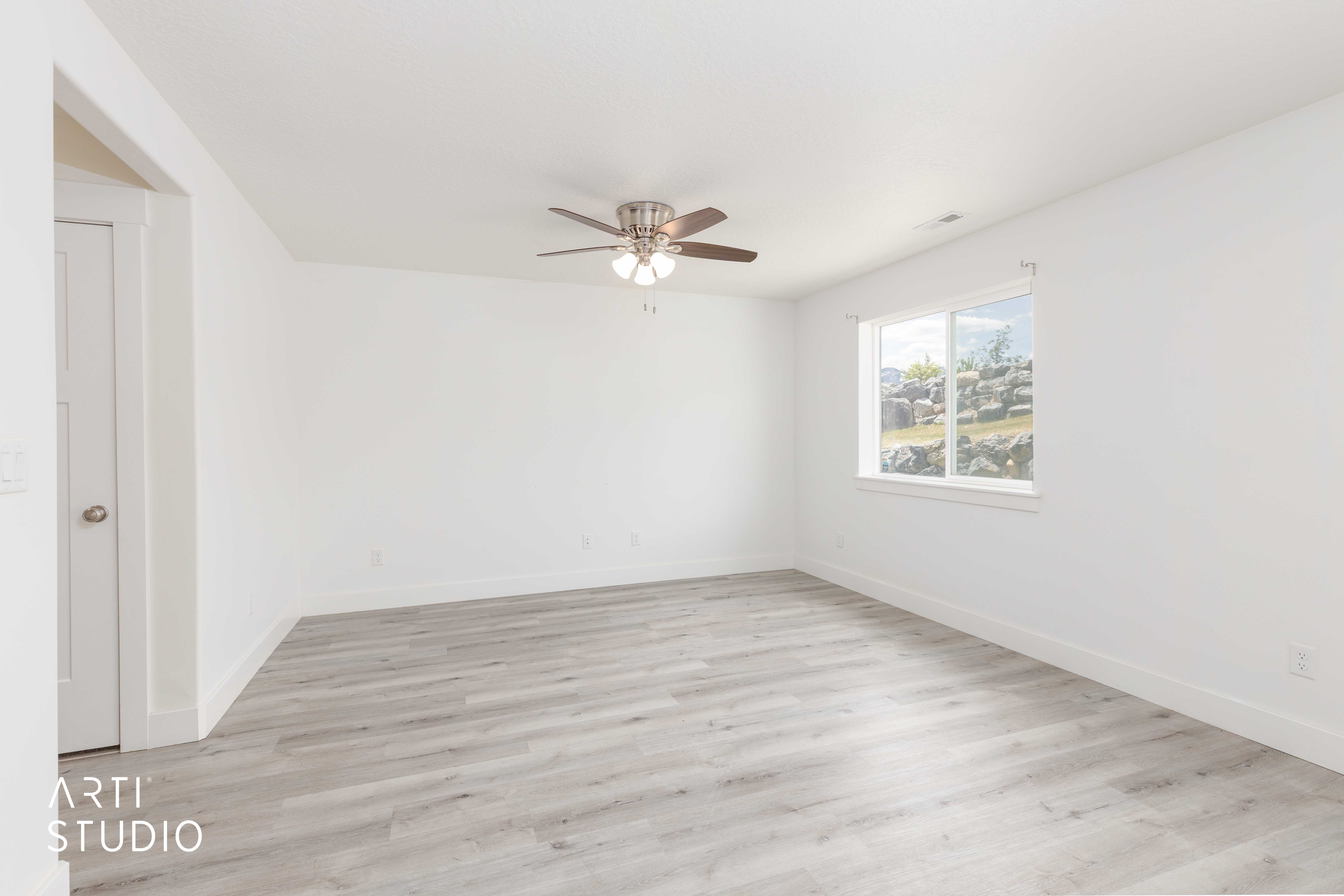 Spacious room featuring light wood-finish flooring, white walls, and a ceiling fan with integrated lighting