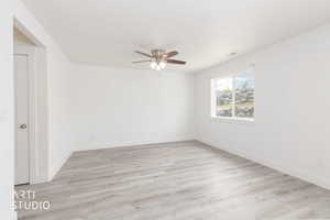 Spacious room featuring light wood-finish flooring, white walls, and a ceiling fan with integrated lighting