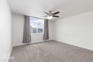 Spacious interior room featuring white walls, grey carpeting, a ceiling fan with integrated lighting, and a large window with grey drapes