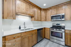 L-shaped kitchen featuring wood cabinetry, light countertops, stainless steel appliances, and wood-finish flooring