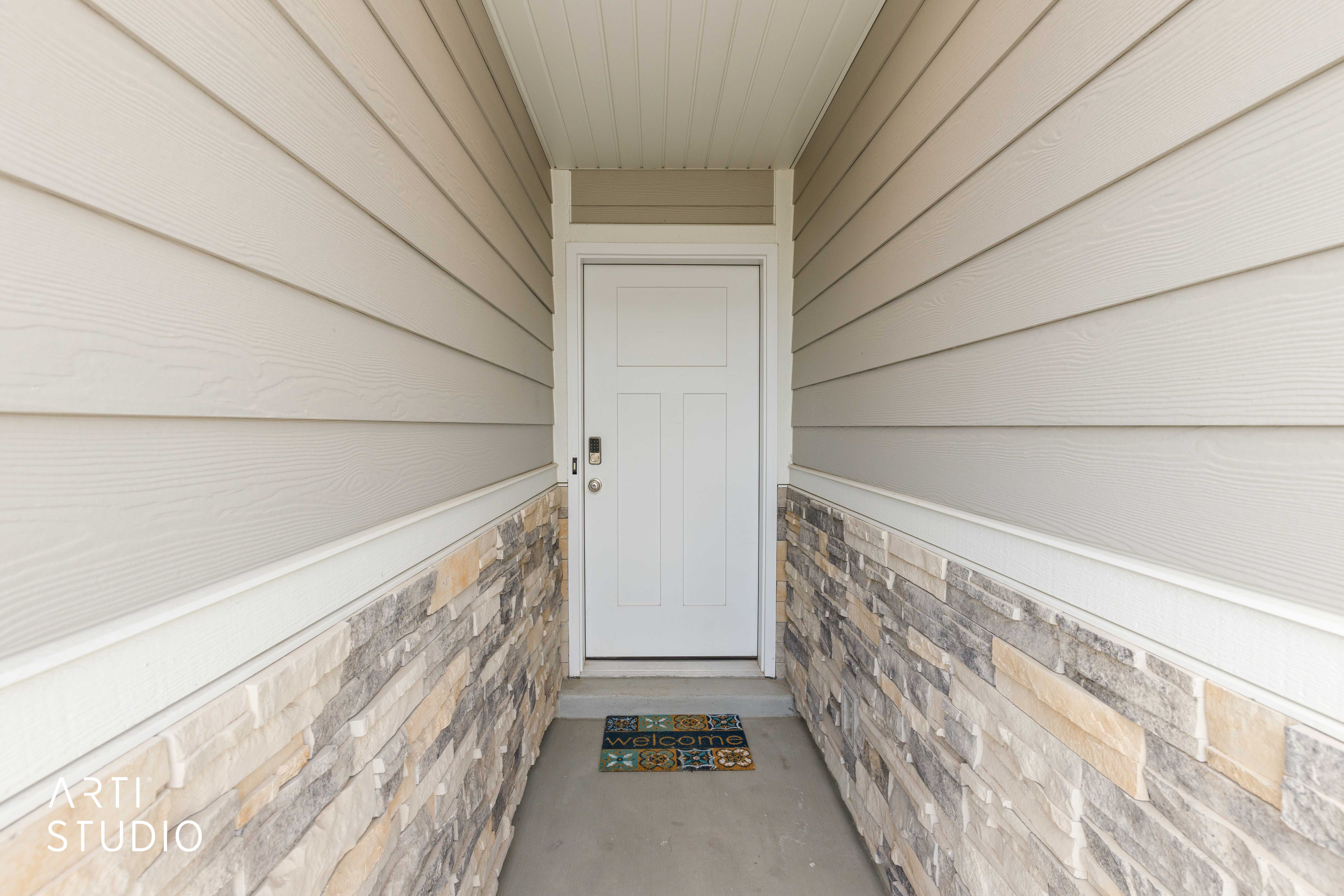 Covered entryway featuring a white panel door, horizontal siding, and a stacked stone veneer accent