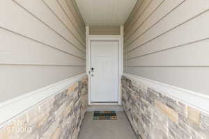 Covered entryway featuring a white panel door, horizontal siding, and a stacked stone veneer accent