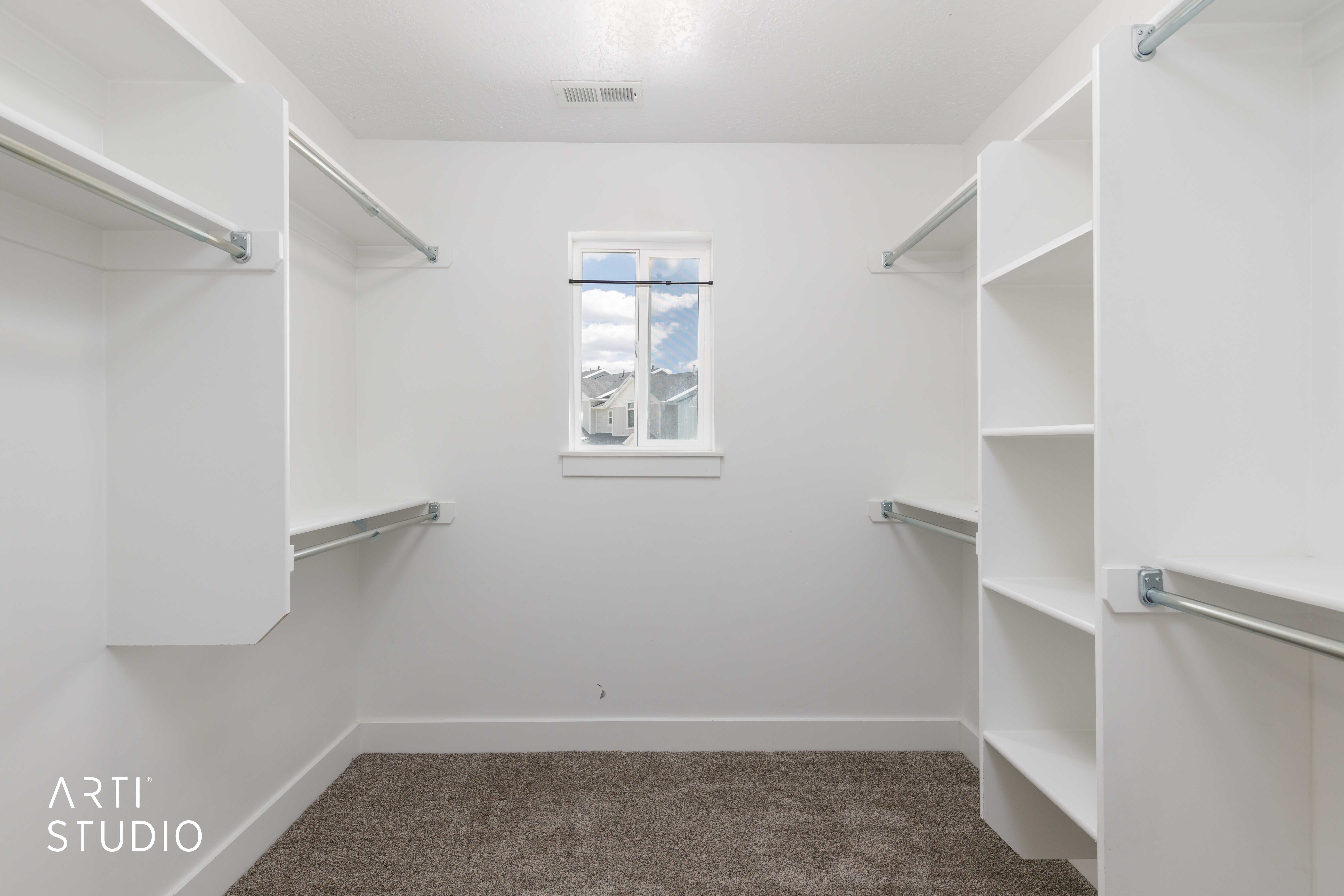 Spacious walk-in closet featuring built-in shelving, multiple hanging rods, and a window for natural illumination