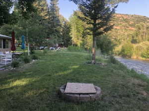 Expansive lawn area featuring a stone-ringed fire pit and mature trees