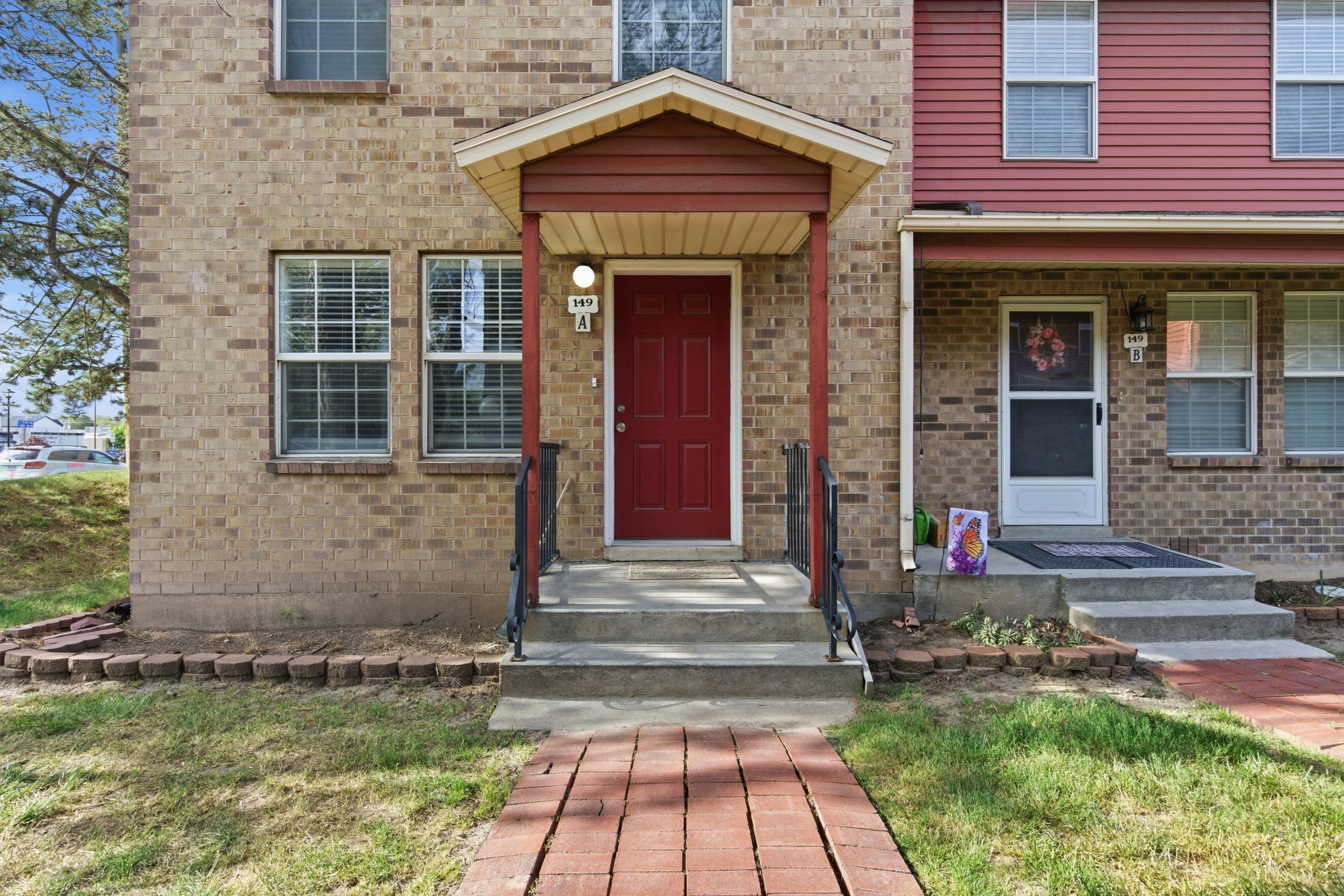 Brick facade property featuring a red entry door with an overhead porch, black wrought iron handrails, and a brick paver walkway