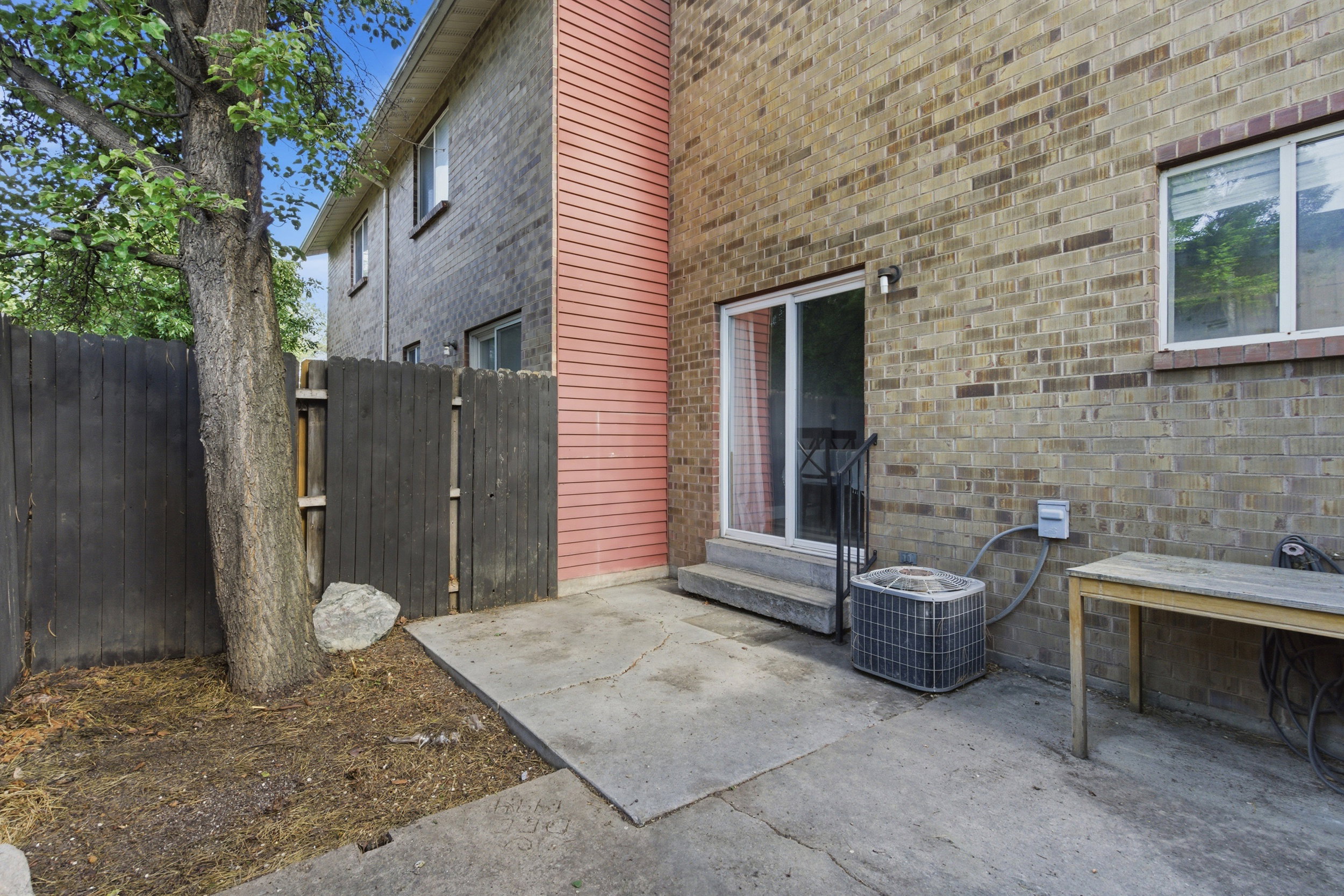 Paved patio area with a sliding glass door entry, brick exterior, and partial privacy fencing