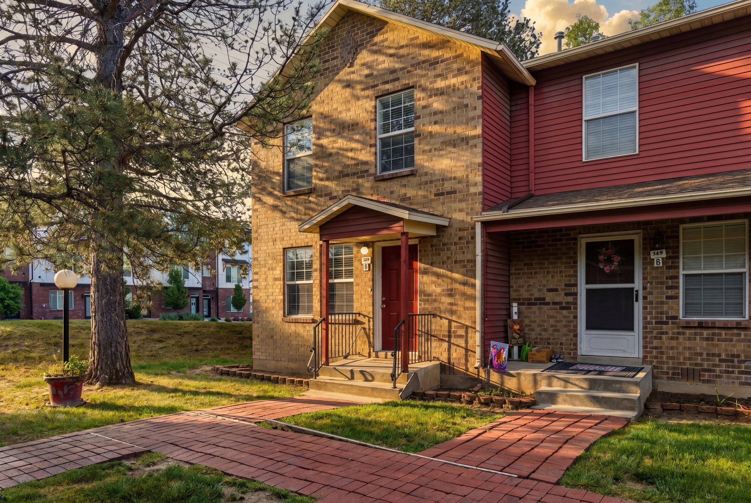 Two-story townhome featuring a brick and horizontal siding exterior, a covered entryway with a red door, and a concrete stoop with black metal railings