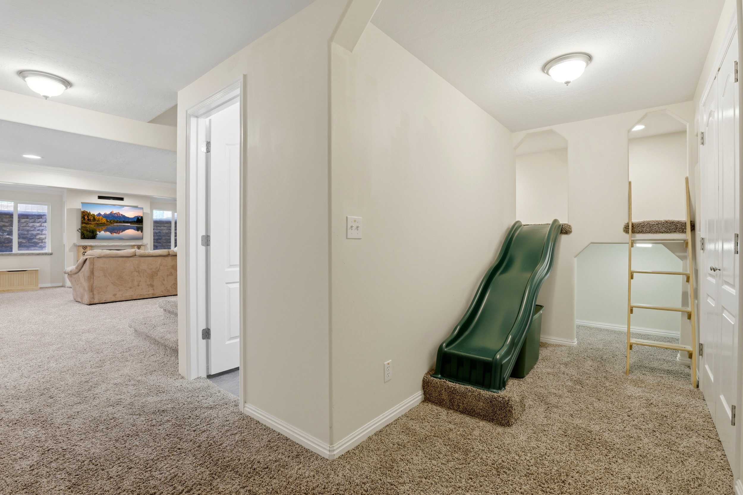 Carpeted hallway with a built-in slide, custom recessed bunk area with ladder, flush-mount lighting, and baseboard molding