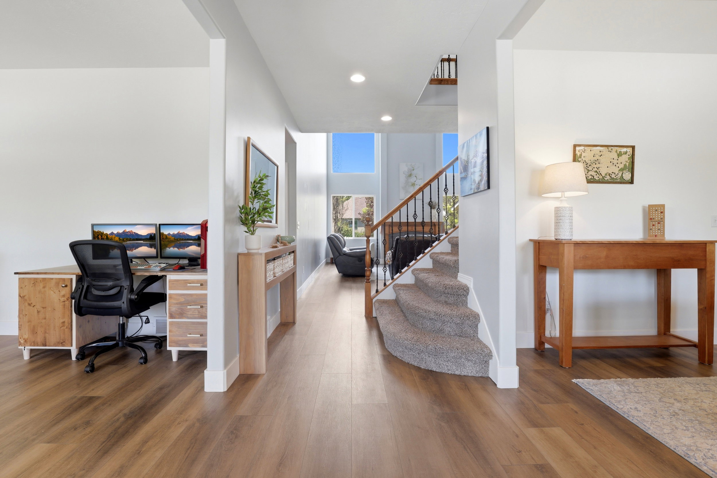 Spacious entryway featuring wood-finish flooring, a curved carpeted staircase with wrought iron balusters, and a dedicated workspace