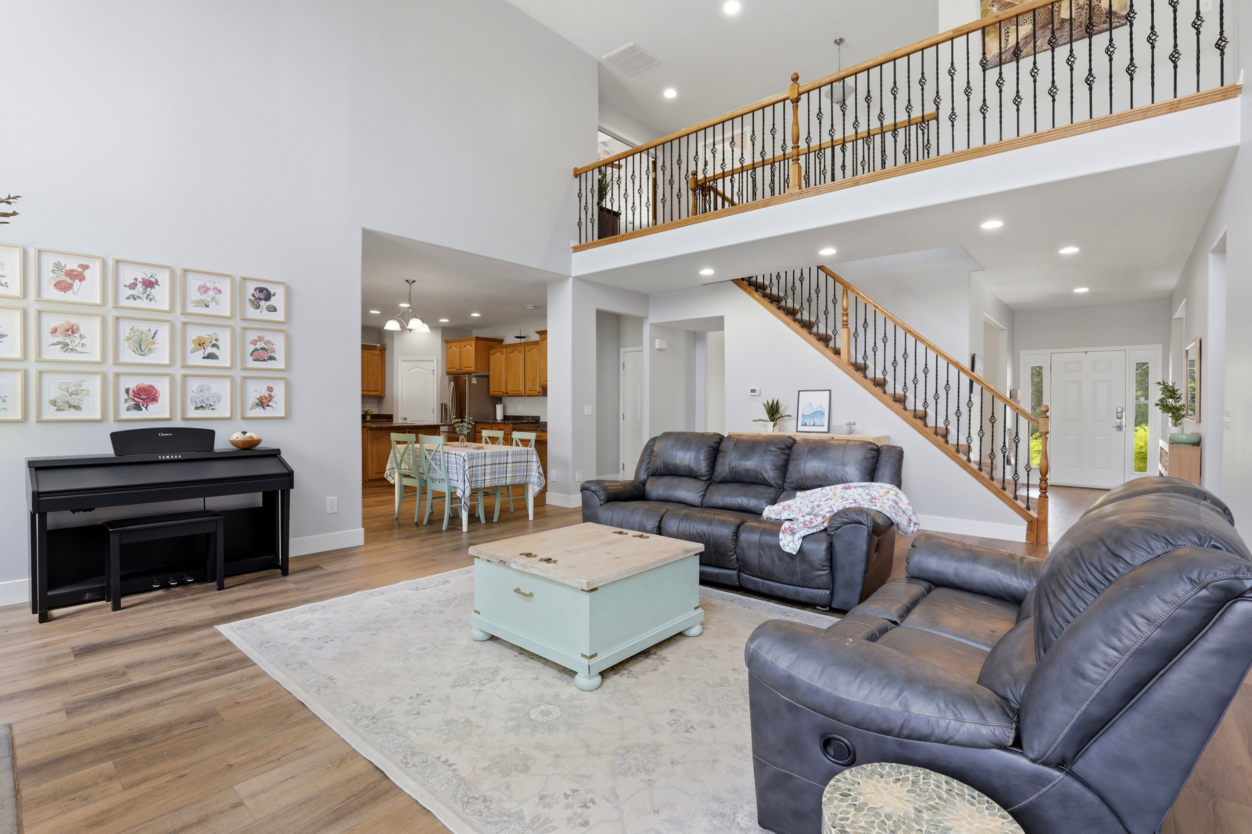 Two-story living area with wood-finish flooring, a grand staircase featuring dark iron balusters and a wood handrail, and an upper-level balcony