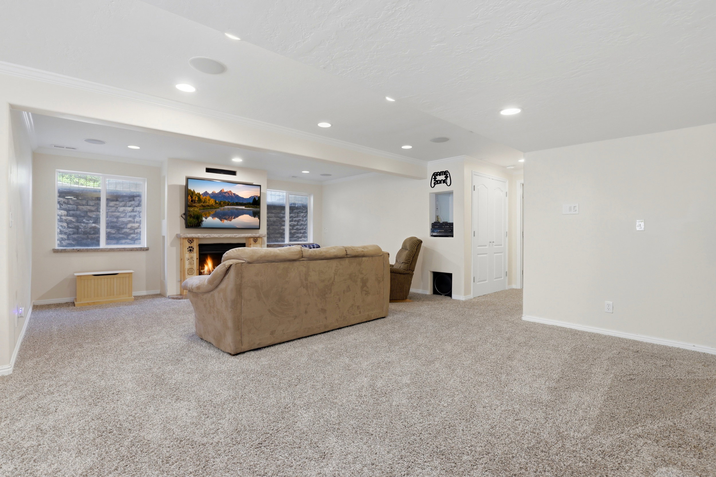 Spacious carpeted room featuring a stone-clad fireplace, built-in media niche, recessed lighting, and dual white trim windows