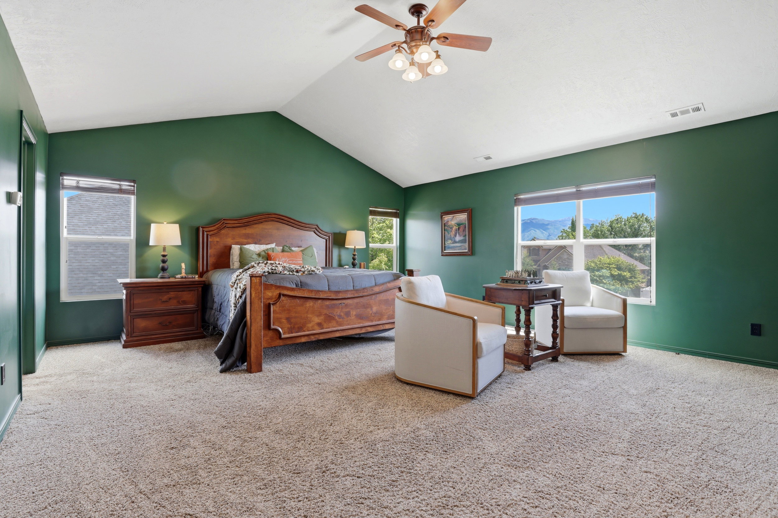 Spacious room featuring vaulted ceilings, a ceiling fan with integrated lighting, recessed windows with blinds, and light-toned carpeting