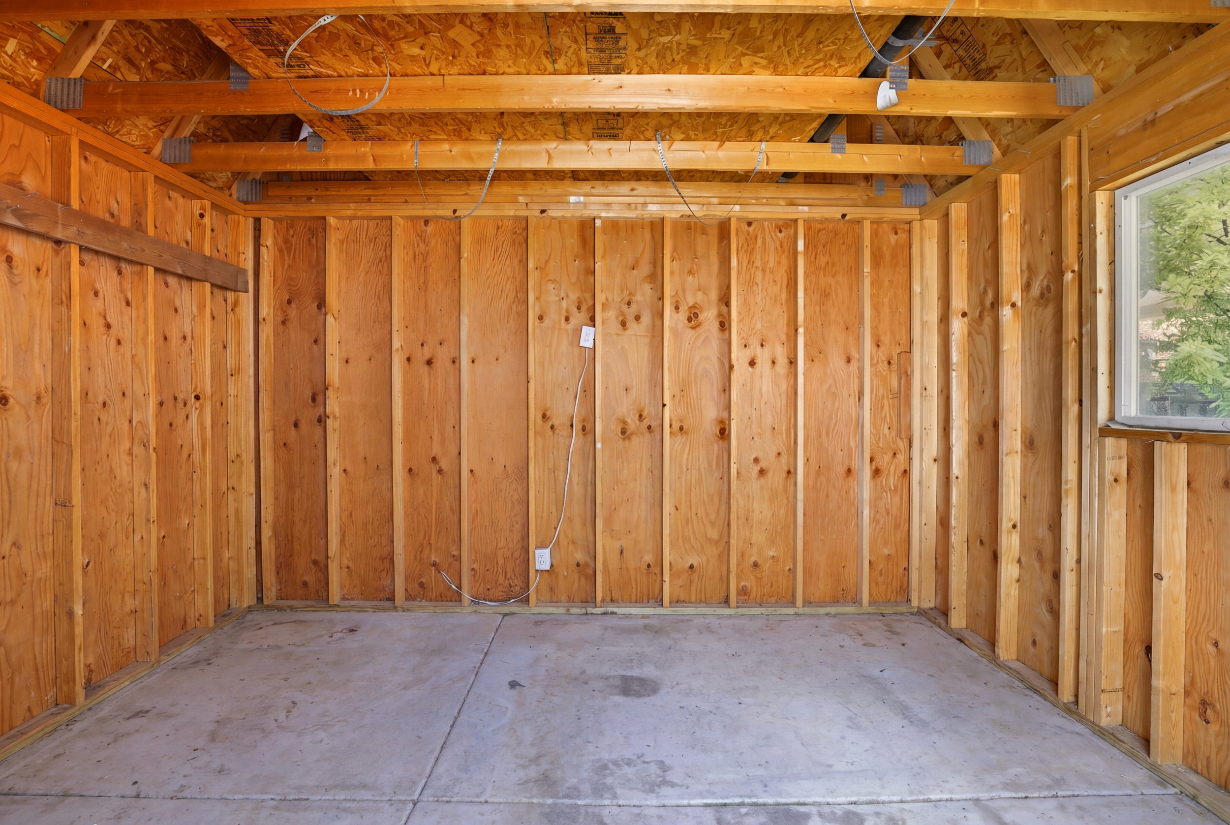 Unfinished interior space featuring exposed wood framing, wood paneling, a concrete floor, and a single window