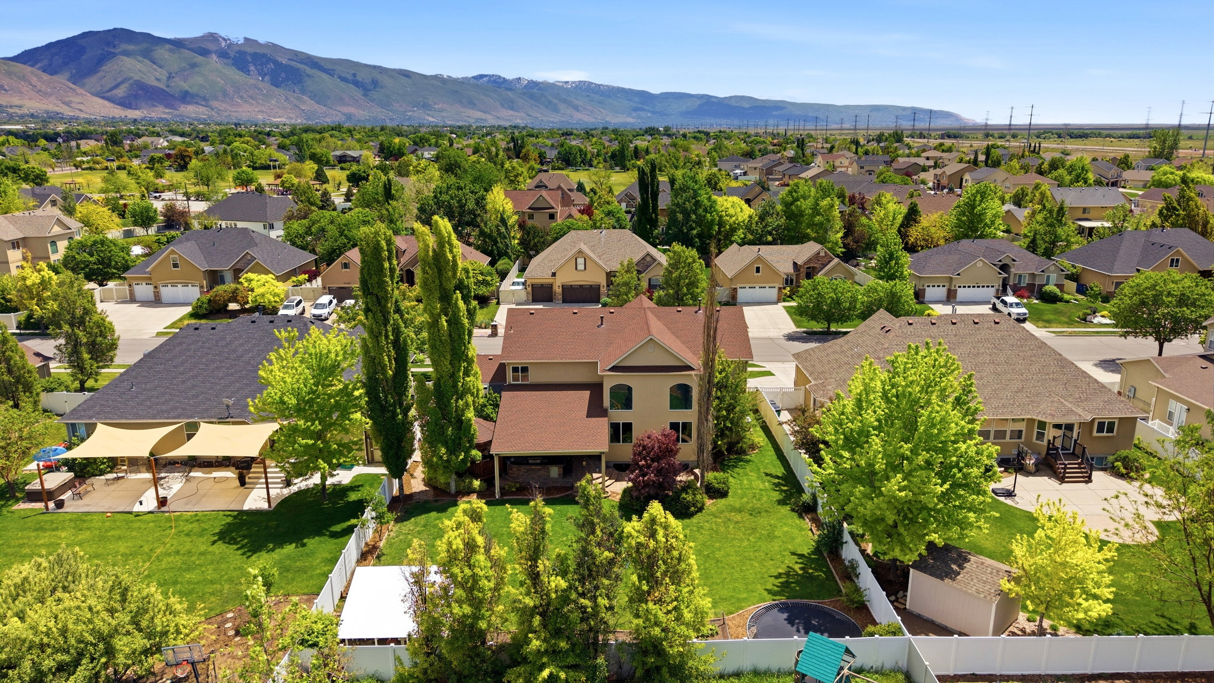 Expansive residential property featuring a large green lawn, mature trees, and a mountain backdrop