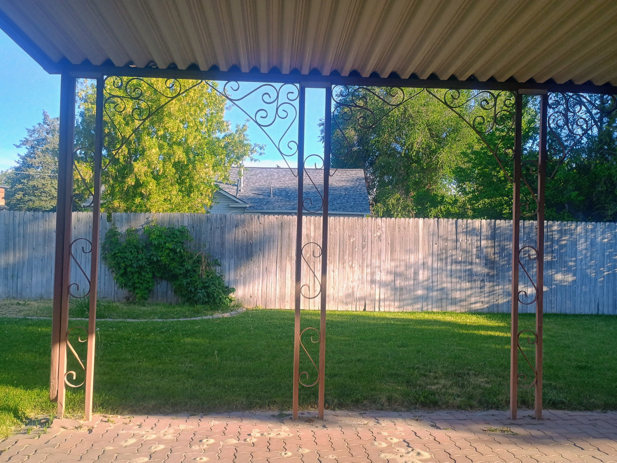 Patio area featuring a corrugated metal roof, decorative wrought iron columns, and brick paver flooring