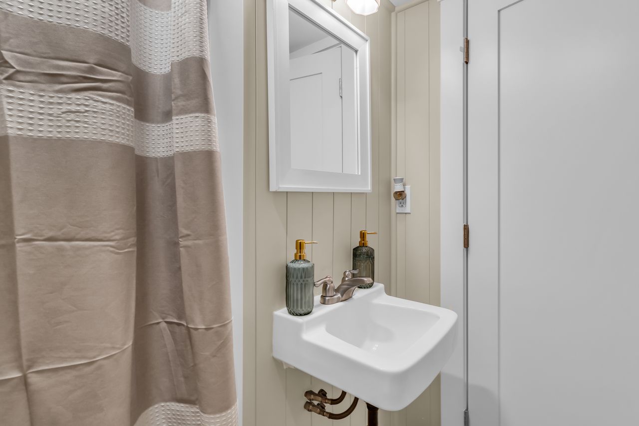 Pedestal sink with chrome faucet, framed mirror, and vertical paneling