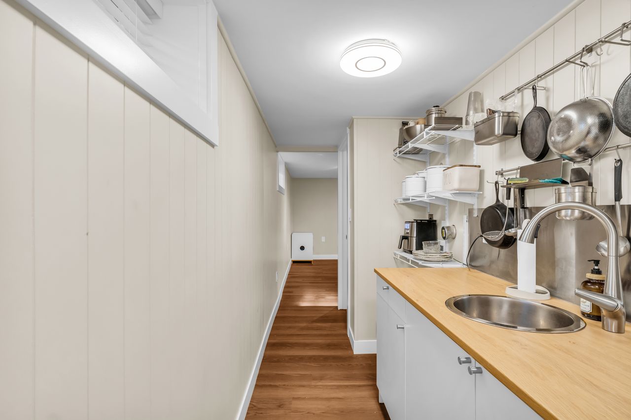 Galley kitchen featuring a stainless steel sink, wood-finish countertops, and white cabinetry