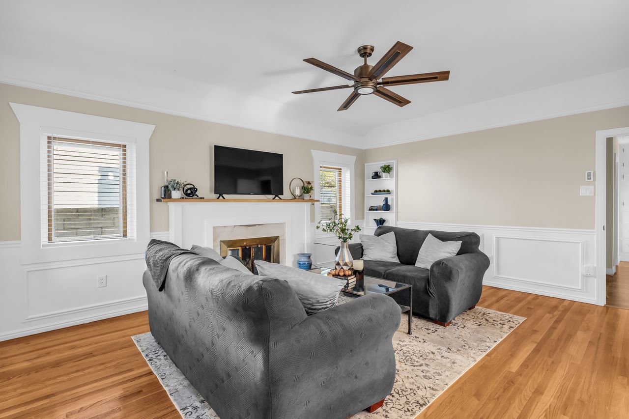 Living room featuring wood-finish flooring, a white fireplace with a mantel, and wainscoting