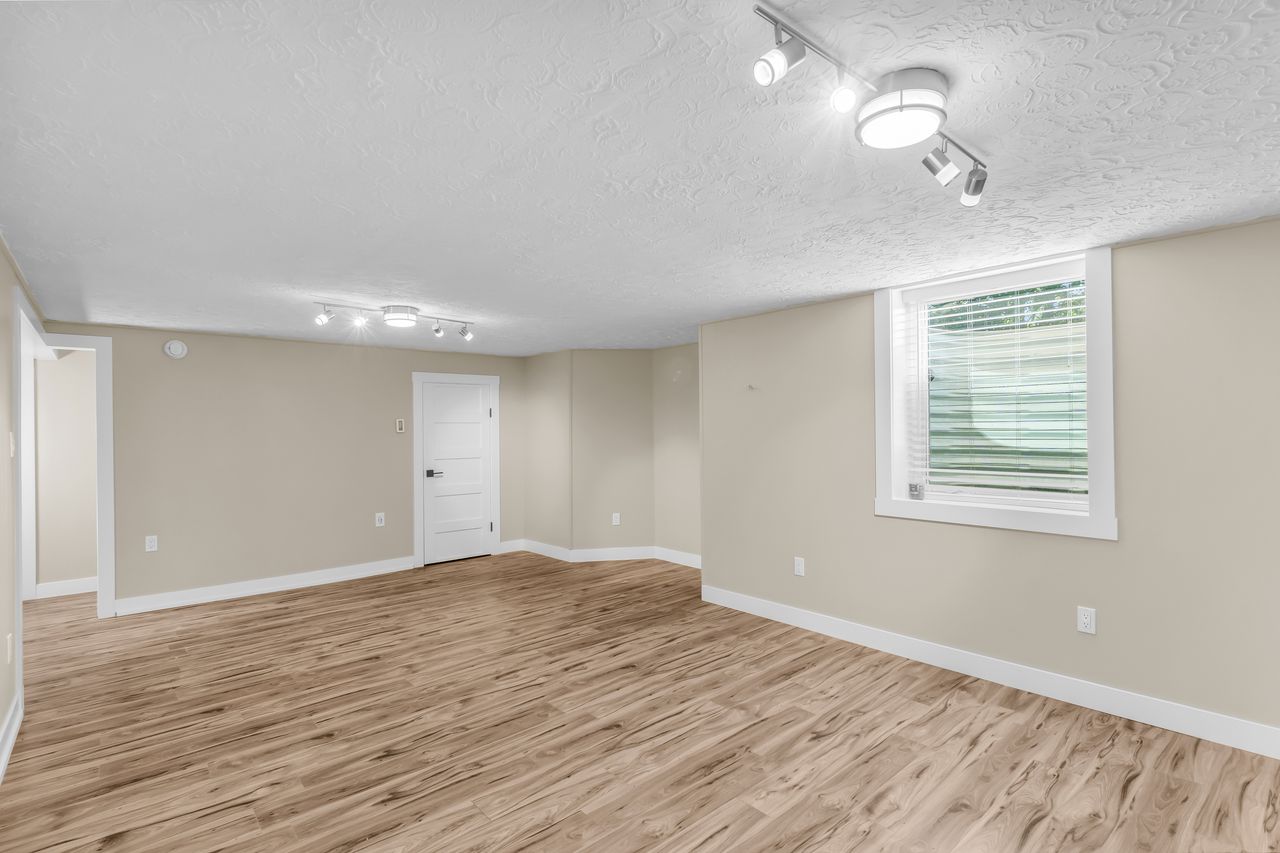 Spacious room featuring wood-finish flooring, neutral-toned walls, and white baseboards