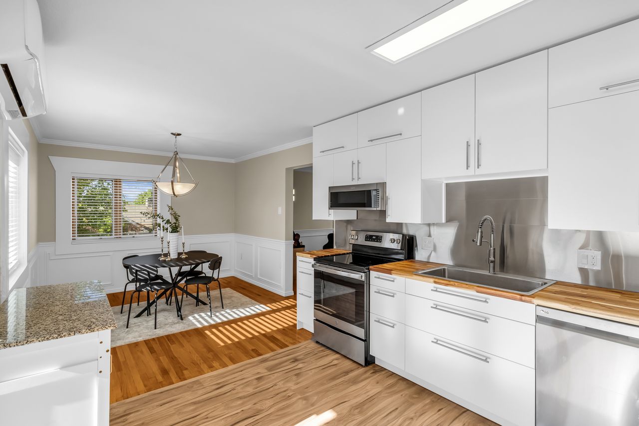 Modern kitchen featuring white cabinetry, wood-finish countertops, stainless steel appliances, and a stainless steel backsplash
