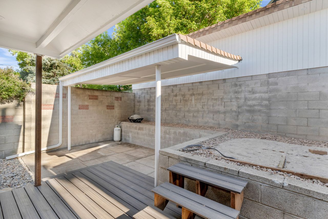 Covered patio area featuring a composite decking surface and a concrete block retaining wall